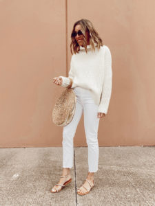 jaime shrayber wearing ivory oversized waffle knit turtleneck sweater with white ankle jeans and round straw bag - spring transition outfit ideas